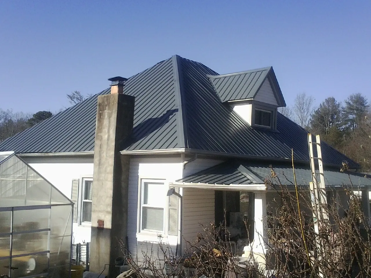 Dark blue standing seam metal roof on a white farmhouse with dormer — Slate & Tile Roof Repair by Roofing Brothers in Irondale