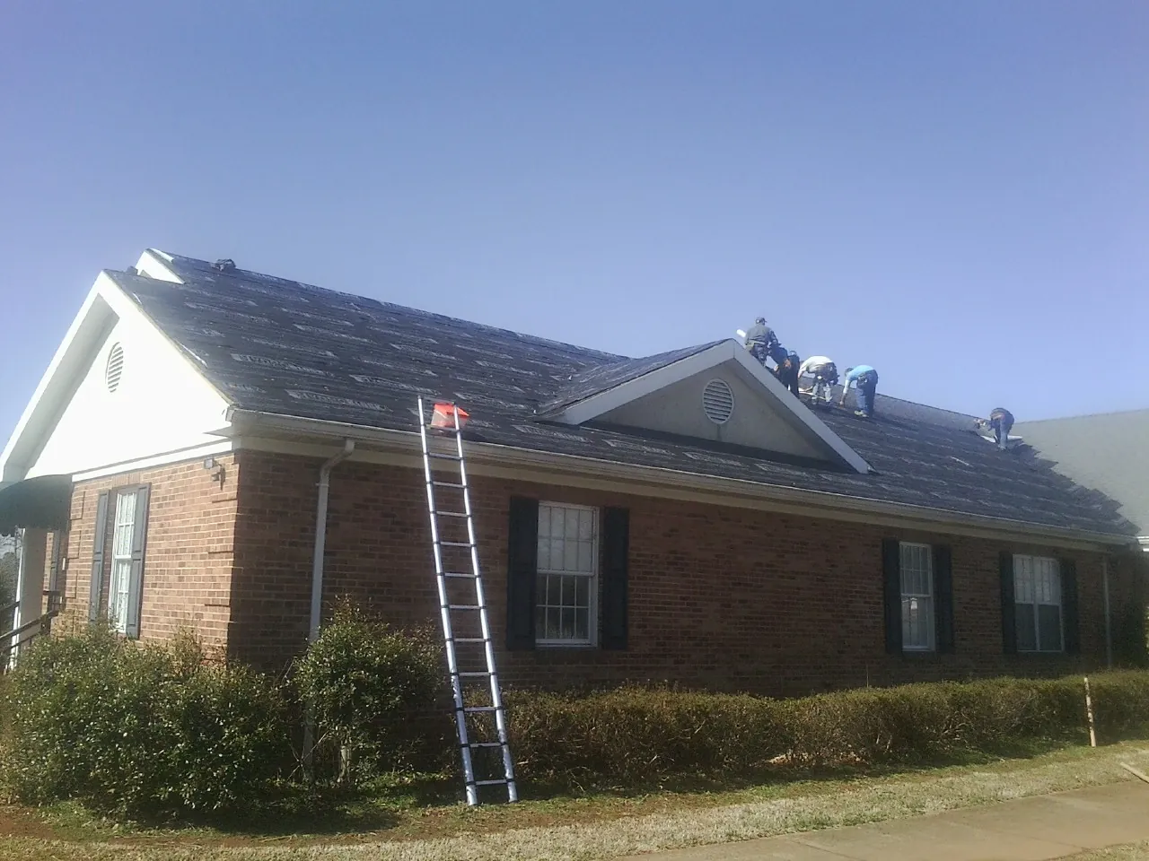 Crew tearing shingles off a brick ranch roof with a ladder set — Metal Roof Repair work by our crew in Irondale
