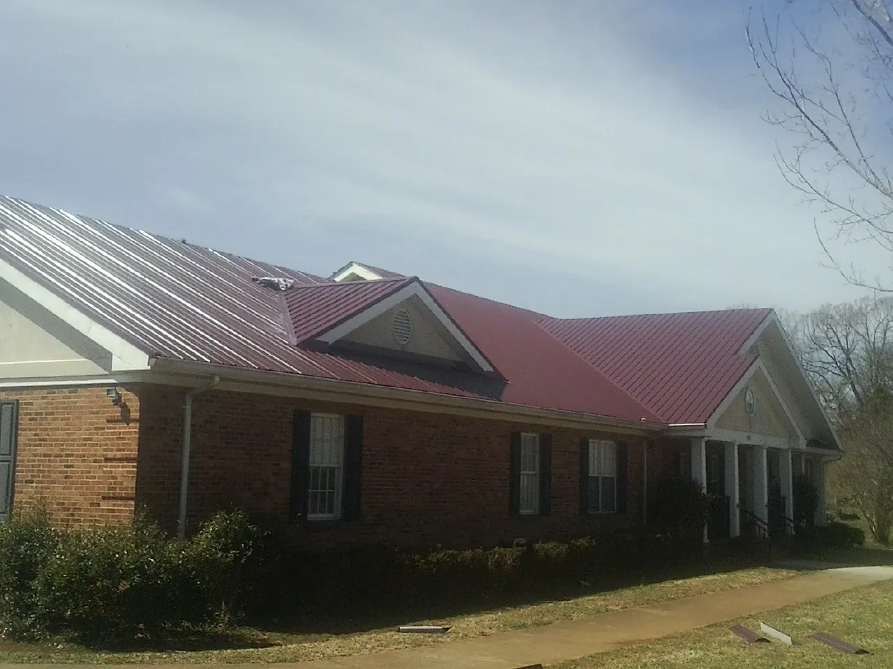 Red metal roof with gabled entries on a long brick building, from a Hail Damage Roof Repair job in Irondale