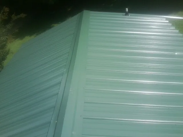 New green metal panels meeting at the ridge of a roof — Flat Roof Repair work by our crew in Irondale