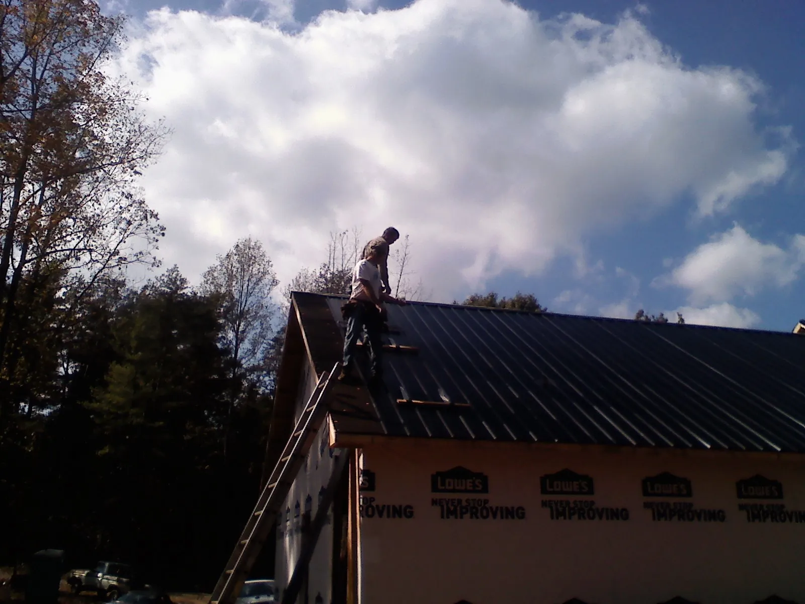 Roofer fastening dark metal panels high against a cloudy sky, from a Roof Inspection job in Irondale
